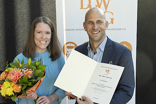 Doktor Tanja Niels steht rechts im Bild mit einem bunten Blumenstraus und einem helblauen Kleid. Professor Ninnemann steht auf der linken Seite im Bild mit der Urkunde für Frau Niels. Beide wirken sehr glücklich und lächeln.